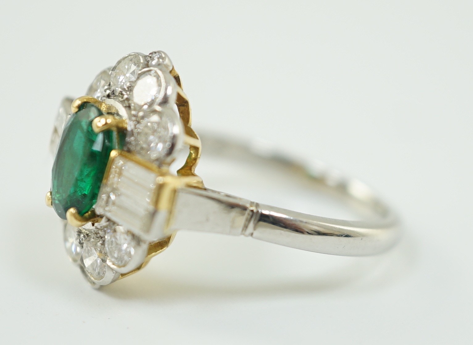 A modern platinum, oval cut emerald and baguette and round cut diamond set cluster ring